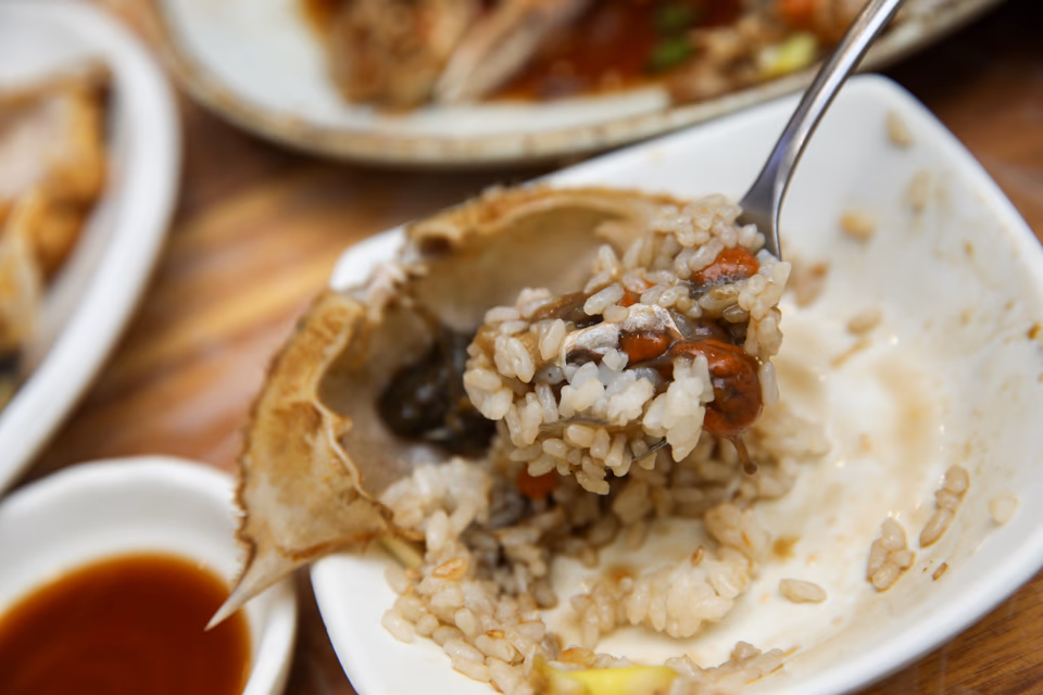 Dark soy brine being poured over whole crabs in a ceramic pot
