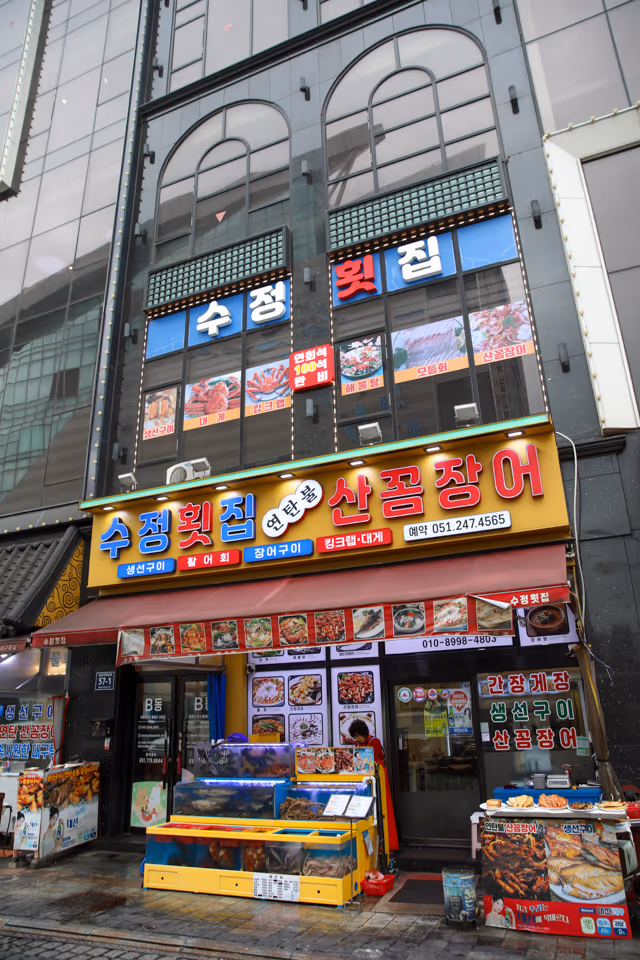 저녁 시간 자갈치해안로 가게 정면, 연탄불 산꼼장어 간판과 활어 수조, 입구 조명