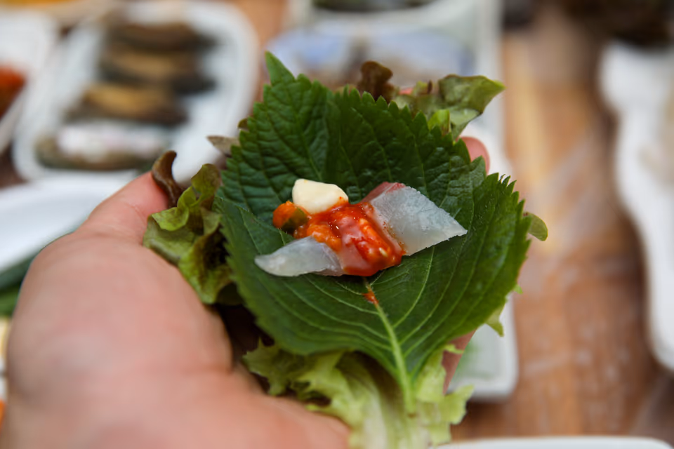 손에 든 깻잎과 상추 위에 흰살 회 한 점과 초장, 마늘을 올린 회 쌈