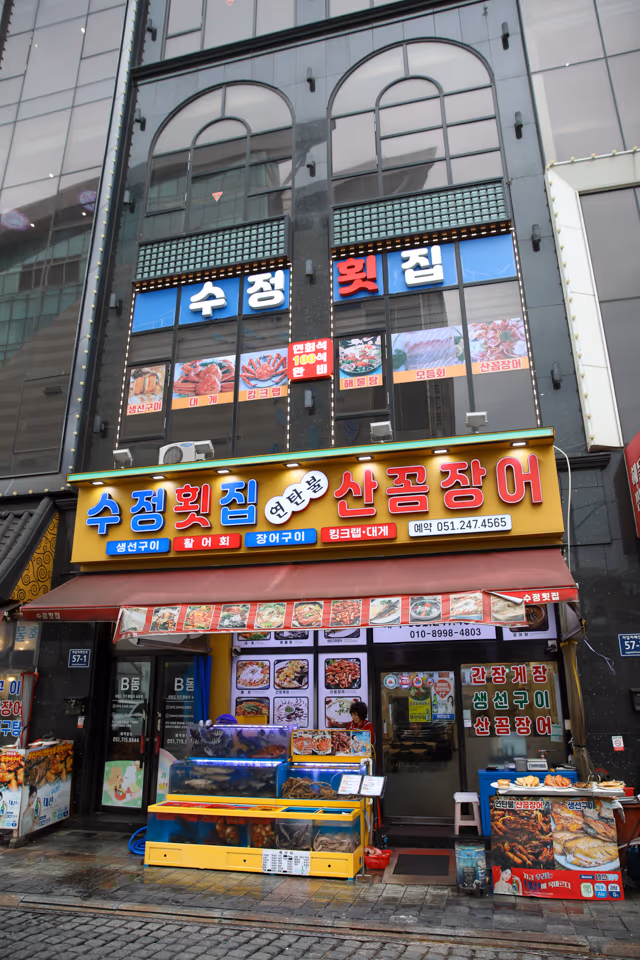 저녁 시간 자갈치해안로 단독 횟집 정면, 연탄불 산꼼장어 간판과 활어 수조, 입구 조명