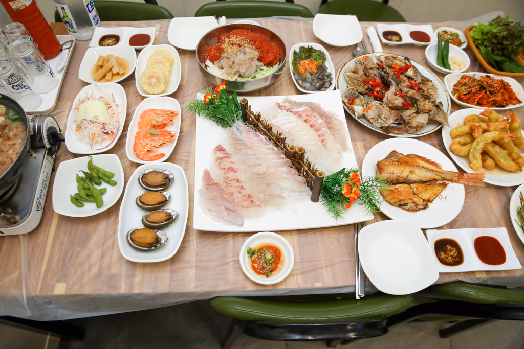 흰살 회, 간장게장, 찐 새우, 전복, 생선구이, 튀김과 반찬이 모두 차려진 상 전경