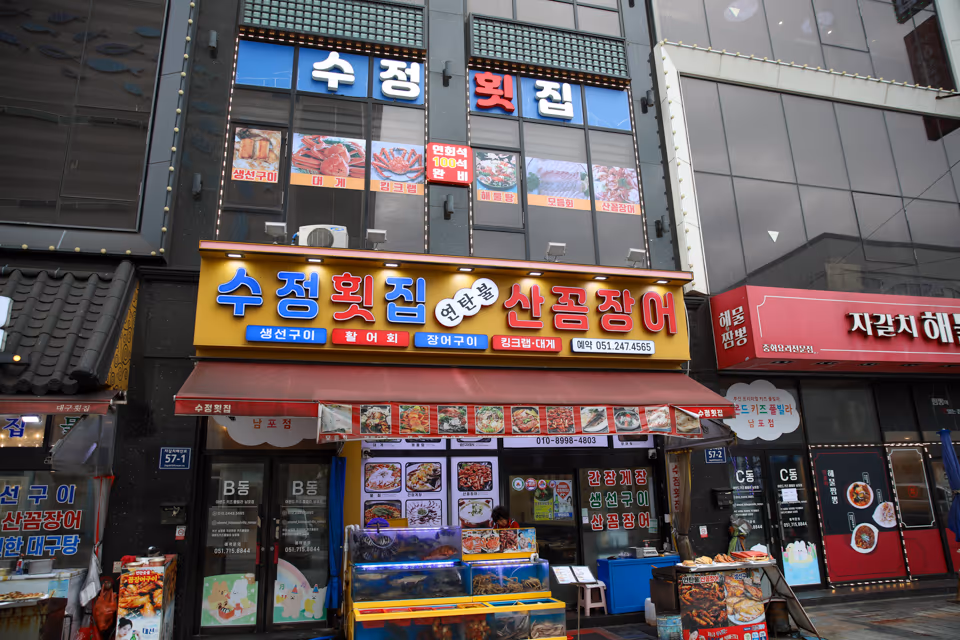 가게 정면 입구, 간판 아래 수족관과 출입문이 나란히 보이는 저녁 풍경