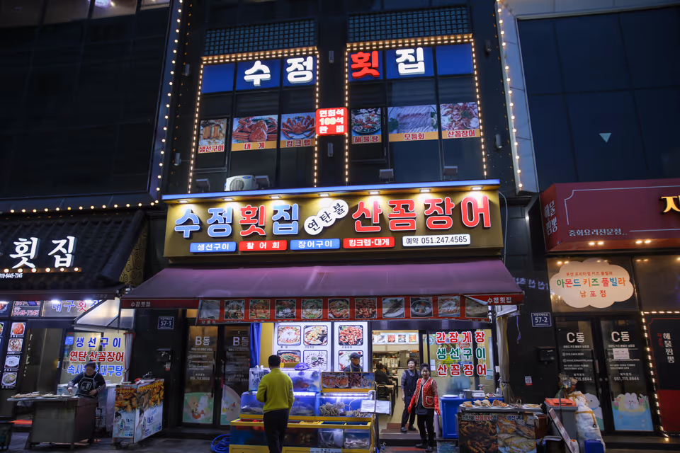 저녁 무렵 자갈치해안로 횟집 정면, 연탄불 산꼼장어 간판 아래 활어 수족관과 입구가 불을 밝힌 모습
