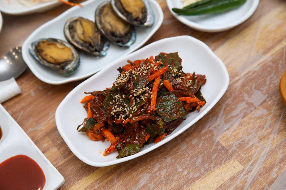 초고추장 양념이 깻잎과 채 썬 채소에 고루 배어든 회무침 접시, 뒤로 전복 접시와 고추