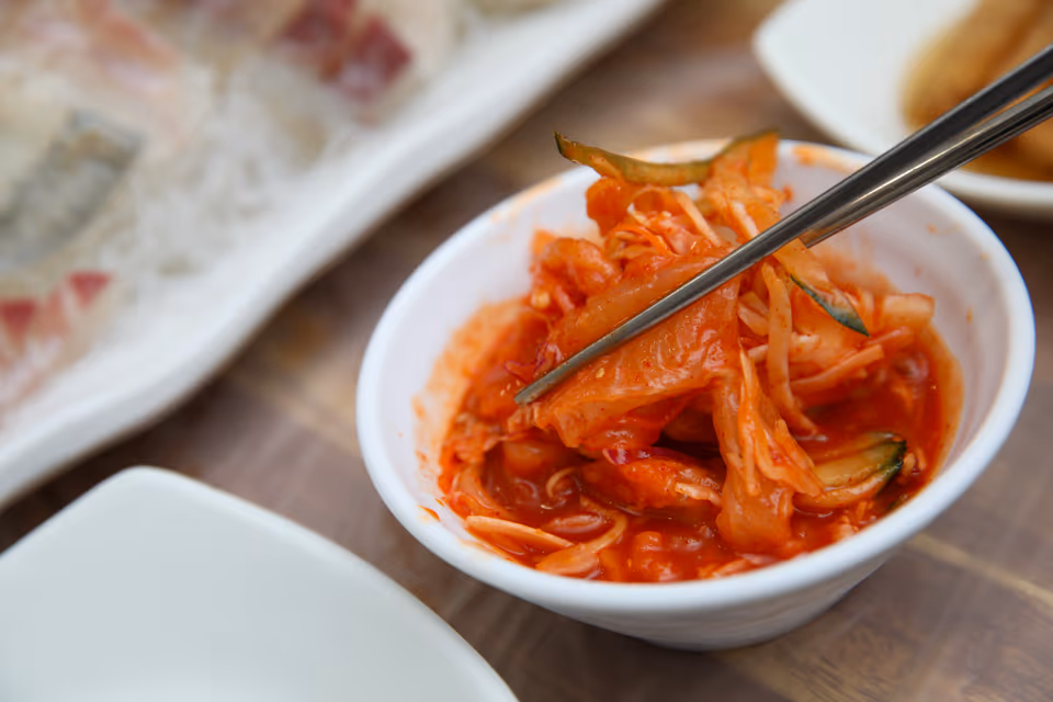 육수를 붓기 전 초고추장에 버무린 물회 재료를 젓가락으로 집는 장면, 채 썬 채소와 회