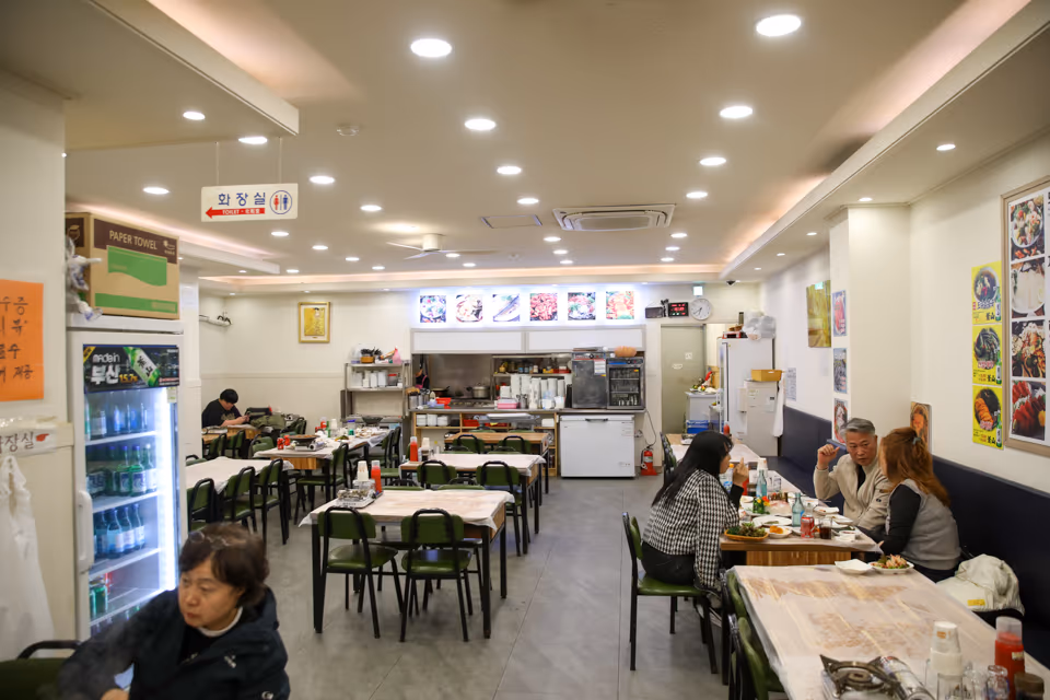 손님들이 식사 중인 1층 홀, 주방 카운터와 냉장고가 보이는 점심 시간 실내