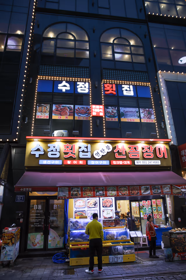 저녁 시간 가게 정면, 연탄불 산꼼장어 간판 아래 입구 앞 수족관과 진열대가 보이는 외관