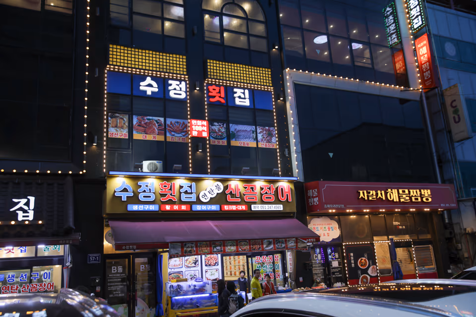 저녁 시간 가게 정면, 불이 켜진 수정횟집 간판과 연탄불 산꼼장어 간판 아래 1층 수족관과 입구