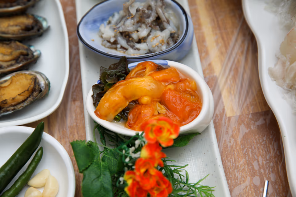 깨를 뿌린 산낙지 접시와 주황빛 멍게 접시가 나란히 놓이고 옆에 껍데기째 담긴 전복과 청양고추·마늘 종지