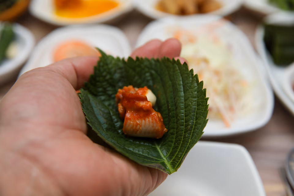 깻잎 위에 올린 양념 꼼장어 한 점과 마늘 클로즈업
