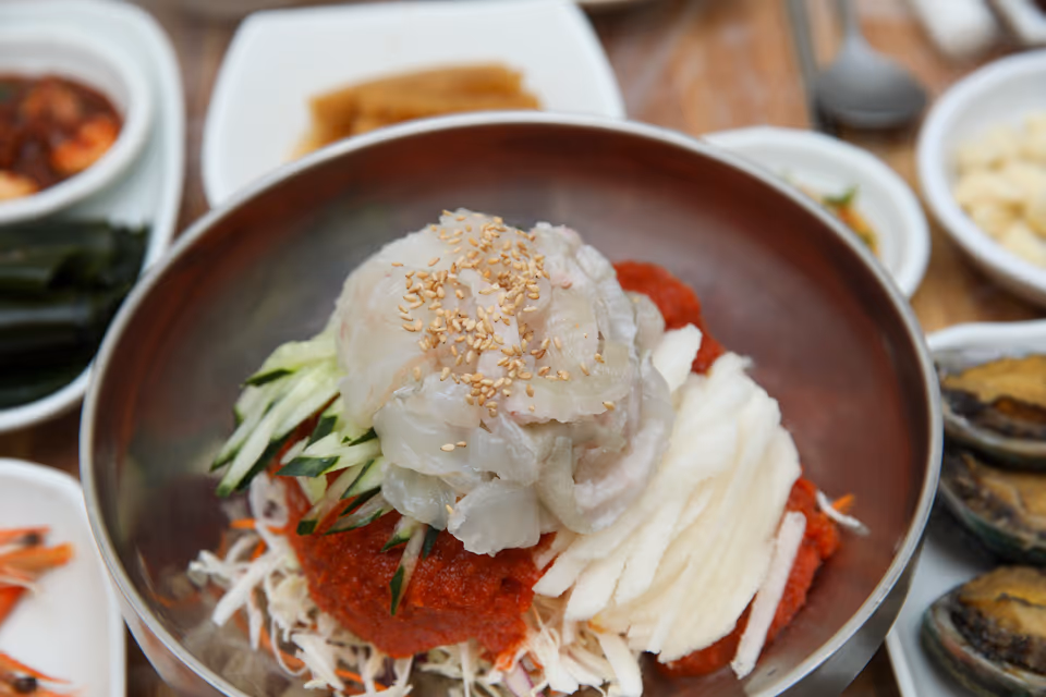 육수 붓기 전 물회 그릇 실사진, 잘게 썬 흰살 회와 오이채 배채 위에 통깨가 뿌려진 모습