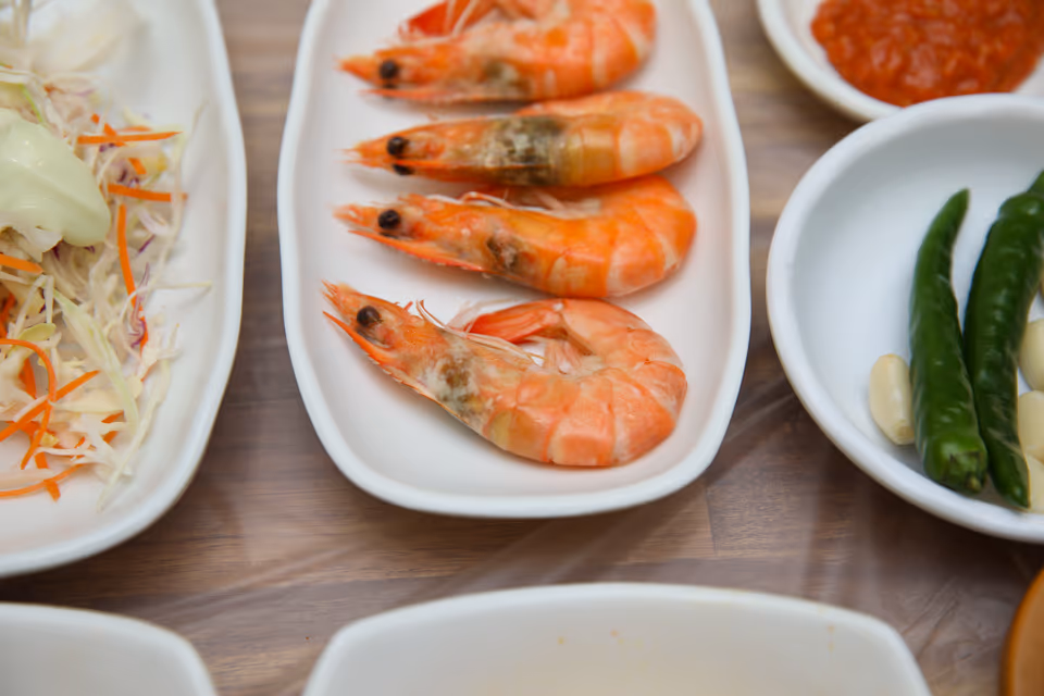 껍질째 익힌 새우 네 마리가 흰 접시에 놓이고 옆으로 양배추 샐러드와 마늘 고추 종지가 보이는 실사진