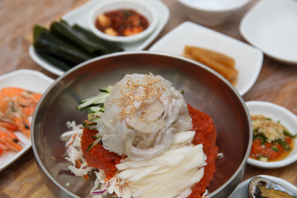 육수 붓기 전 물회 그릇 실사진, 잘게 썬 흰살 회와 오이채 배채 위에 통깨가 뿌려진 모습