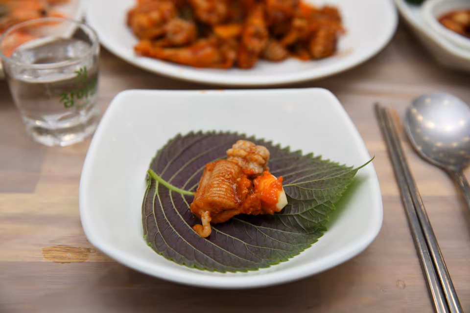 깻잎 위에 양념 꼼장어 한 점과 마늘을 올린 쌈, 뒤로 양념 꼼장어 접시와 소주잔